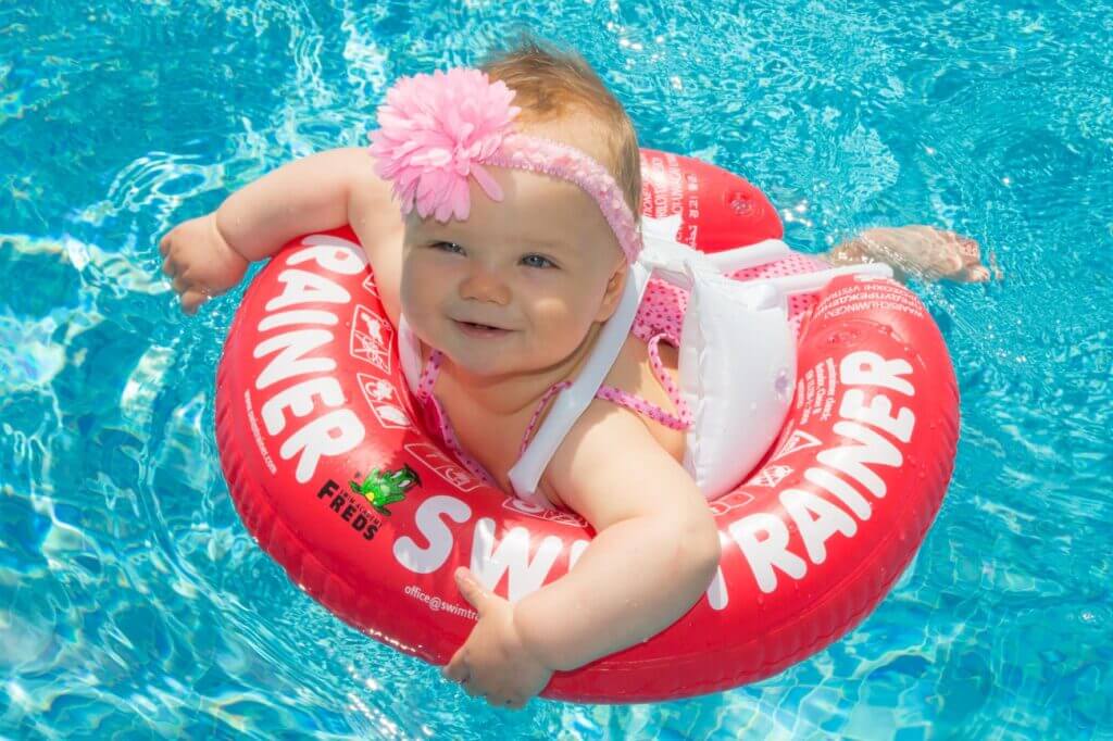 Un bébé souriant qui nage avec une bouée Swimtrainer rouge.