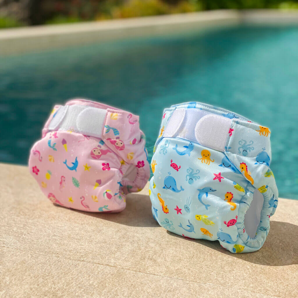 Maillot-couches lavables Swim Nappy rose et bleu devant une piscine.