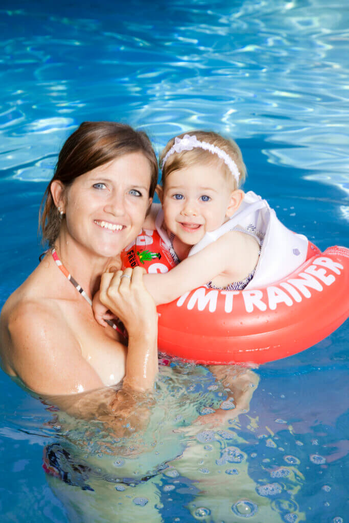 Une mère et son enfant qui nage avec une bouée Swimtrainer rouge dans une piscine.