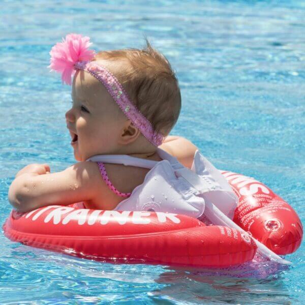 Petite fille souriante nageant avec une bouée Swimtrainer classique rouge.